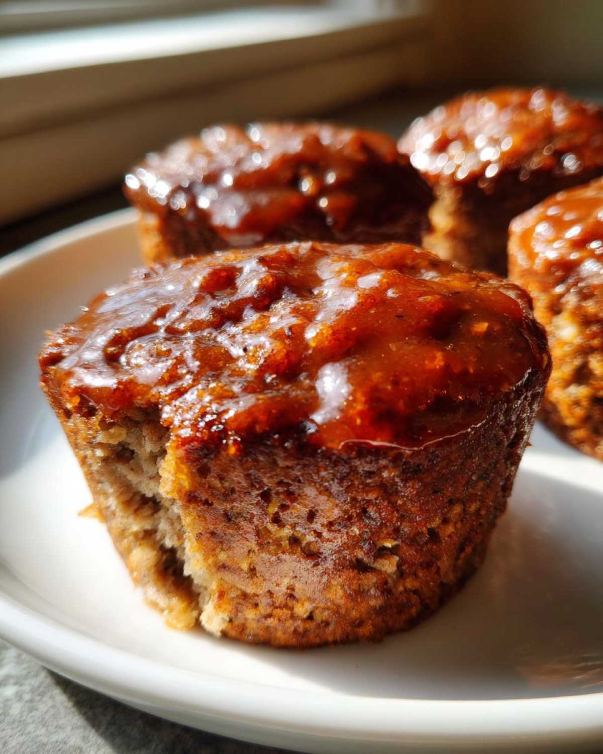 Close-up of a single, moist mini meatloaf topped with a shiny brown glaze, sitting on a white plate.