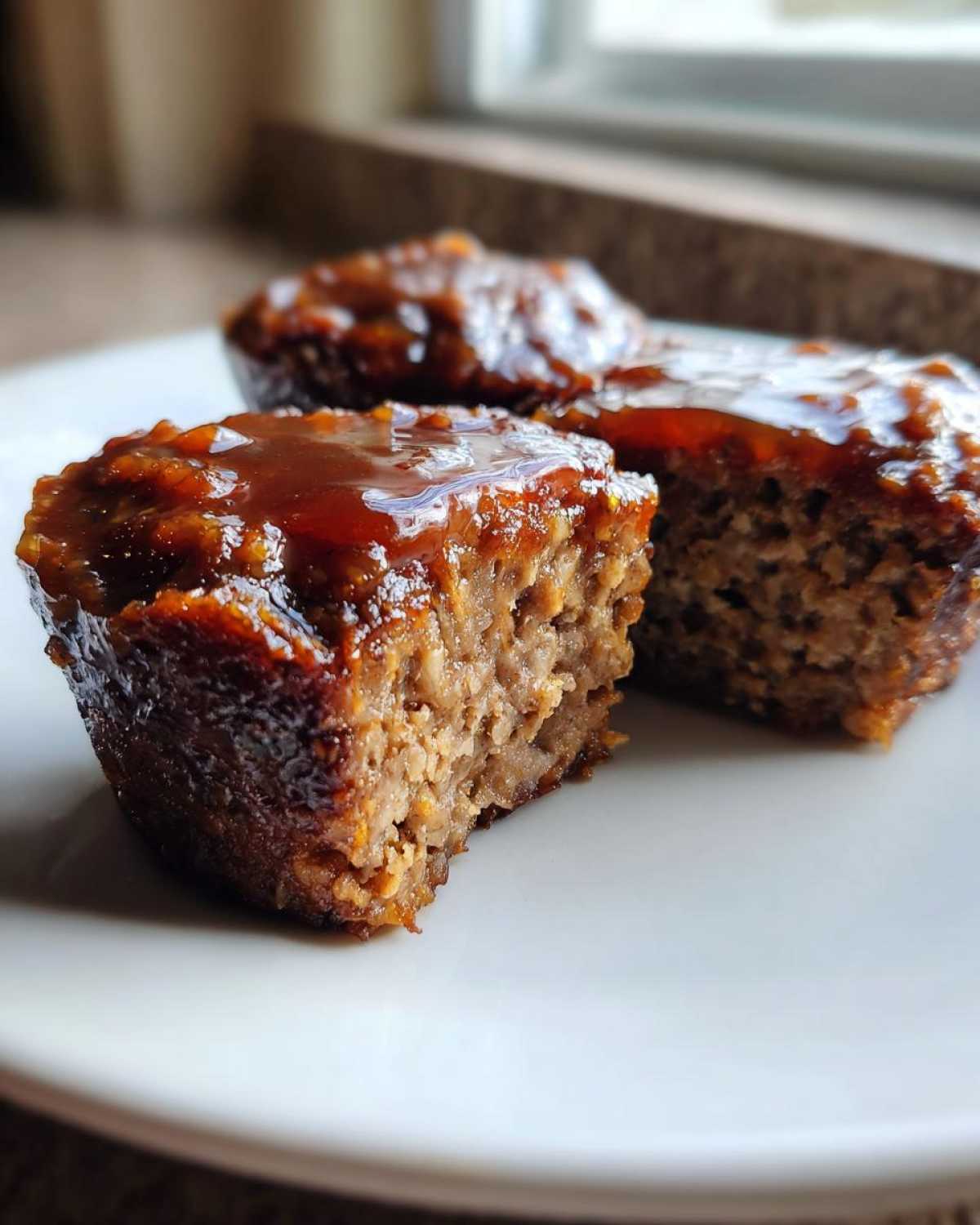 Close-up of a glazed mini meatloaf cut in half, showing the texture of the mini meatloaf on a white plate.