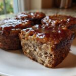 Close-up of four individual mini meatloaf portions, one cut open, showing a thick, shiny glaze.