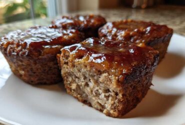 Close-up of four individual mini meatloaf portions, one cut open, showing a thick, shiny glaze.