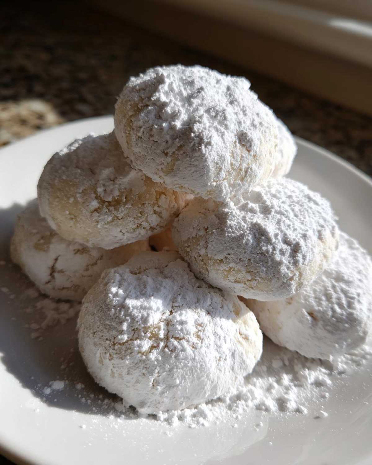 A close-up stack of Gluten-Free Lemon Meltaway Cookies heavily dusted with white powdered sugar on a white plate.