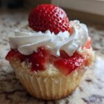 Close-up of a single Gluten-Free Strawberry Shortcake Cupcake topped with whipped cream and a whole fresh strawberry.