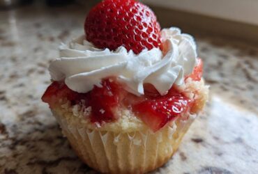 Close-up of a single Gluten-Free Strawberry Shortcake Cupcake topped with whipped cream and a whole fresh strawberry.