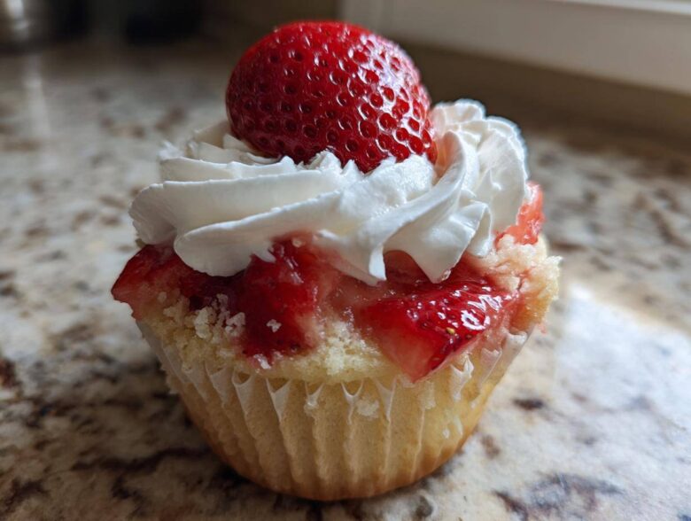 Close-up of a single Gluten-Free Strawberry Shortcake Cupcake topped with whipped cream and a whole fresh strawberry.
