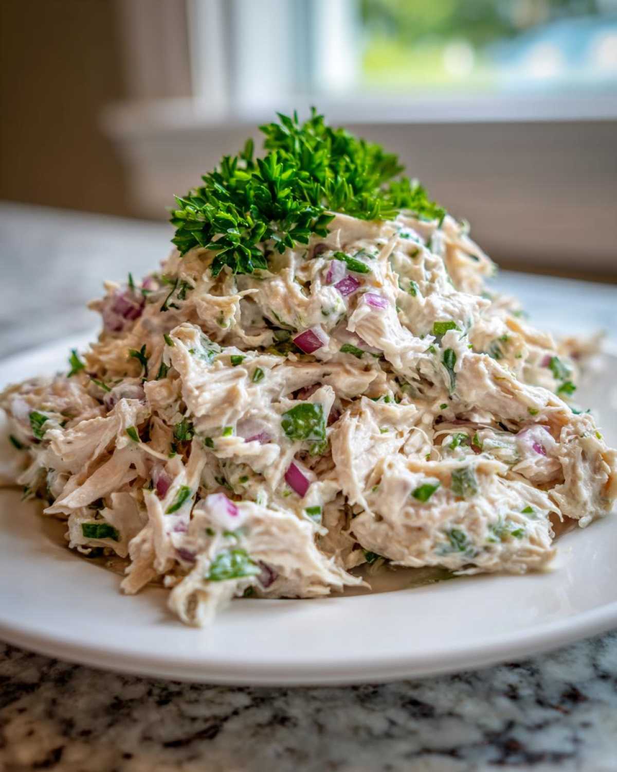 A mound of creamy greek yogurt chicken salad mixed with red onion and herbs, topped with fresh parsley.