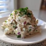 A mound of creamy greek yogurt chicken salad mixed with red onion and celery, topped with fresh parsley.