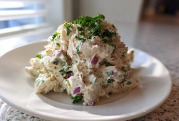 A mound of creamy greek yogurt chicken salad mixed with red onion and celery, topped with fresh parsley.
