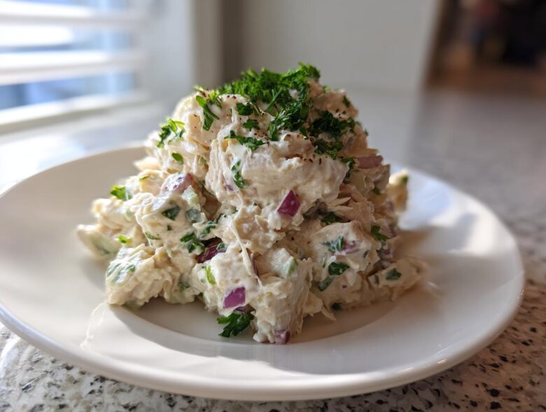 A mound of creamy greek yogurt chicken salad mixed with red onion and celery, topped with fresh parsley.