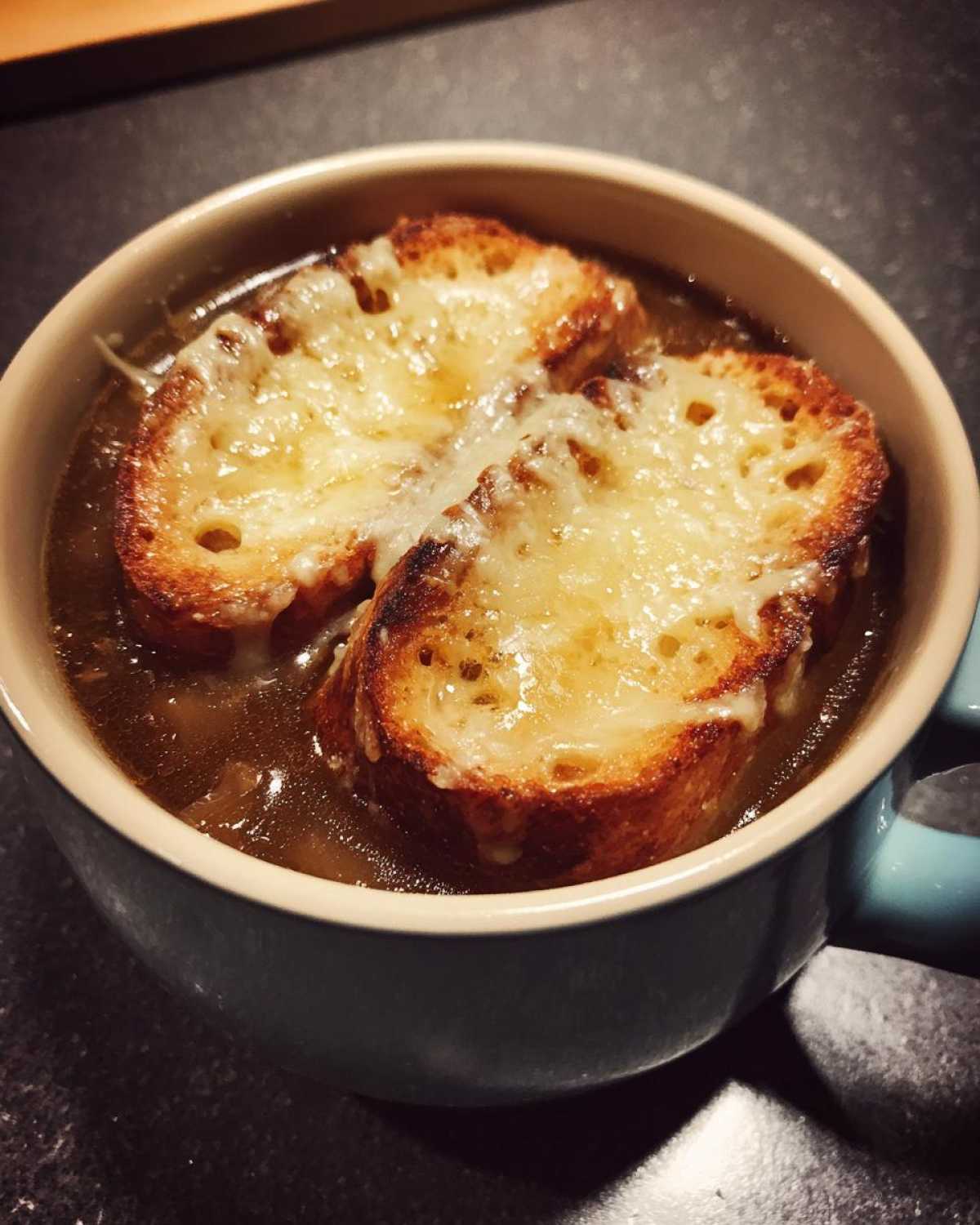 Close-up of a bowl of rich Instant Pot French Onion Soup topped with two slices of toasted bread and melted Gruyère cheese.