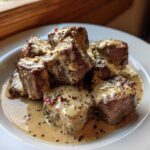 A serving of Keto Creamy Peppercorn Steak Bites drenched in a rich, speckled sauce on a white plate.