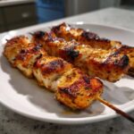 Close-up of juicy, charred Keto Lemon Garlic Chicken Skewers resting on a white plate.