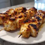 Close-up of three perfectly grilled Keto Lemon Garlic Chicken Skewers resting on a white plate.