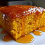 Close-up of a moist slice of bright orange sweet potato cornbread topped with a shiny, dripping glaze.