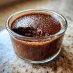 A close-up of rich, dark chocolate mousse in a small glass dish with a spoonful removed.