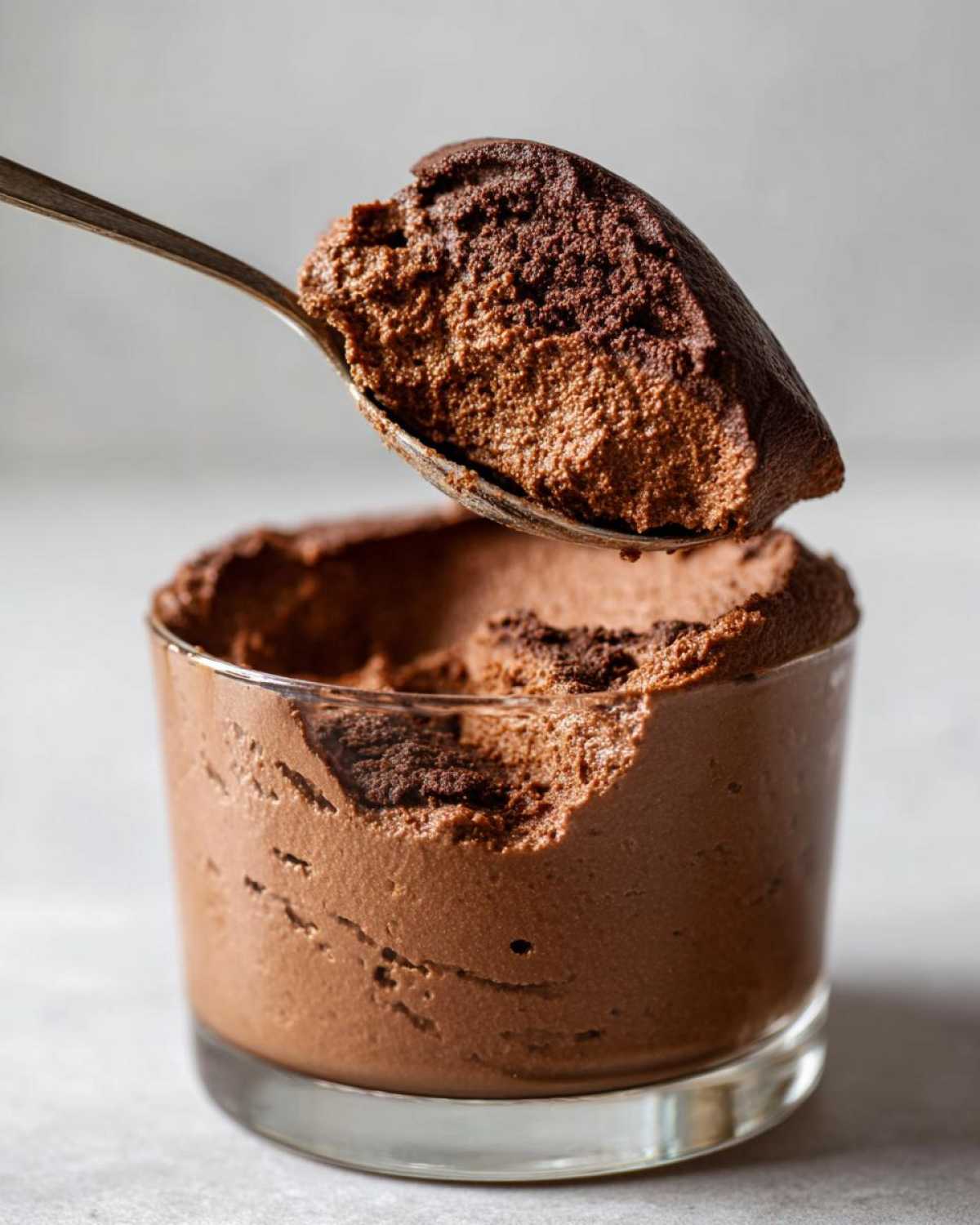 A spoonful of rich, airy chocolate mousse being lifted from a glass serving dish.