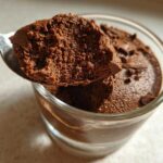 A spoonful of rich, airy chocolate mousse being lifted from a glass cup.