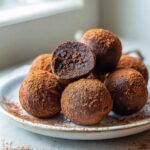 A pile of rich No-Bake Chocolate Orange Truffles dusted heavily with cocoa powder, one cut open.