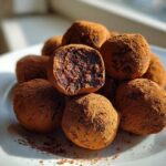 A pile of rich, cocoa-dusted No-Bake Chocolate Orange Truffles, with one cut in half showing the dense interior.