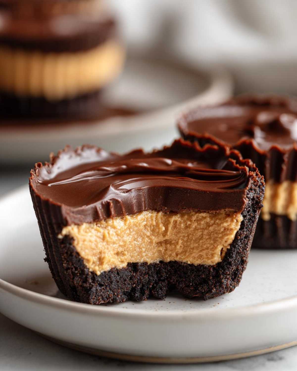 Close-up of a No-Bake Chocolate Peanut Butter Cheesecake Cup cut in half showing the dark crust, peanut butter filling, and chocolate topping.