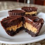 A close-up of a No-Bake Chocolate Peanut Butter Cheesecake Cup cut in half, showing the dark crust, peanut butter filling, and chocolate topping.