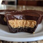 A cross-section view showing the layers of a No-Bake Chocolate Peanut Butter Cheesecake Cup: chocolate crust, peanut butter filling, and chocolate topping.