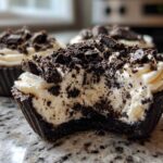 A close-up view of a No-Bake Cookies and Cream Pie Cup with a bite taken out, showing the creamy filling and chocolate cookie crust.