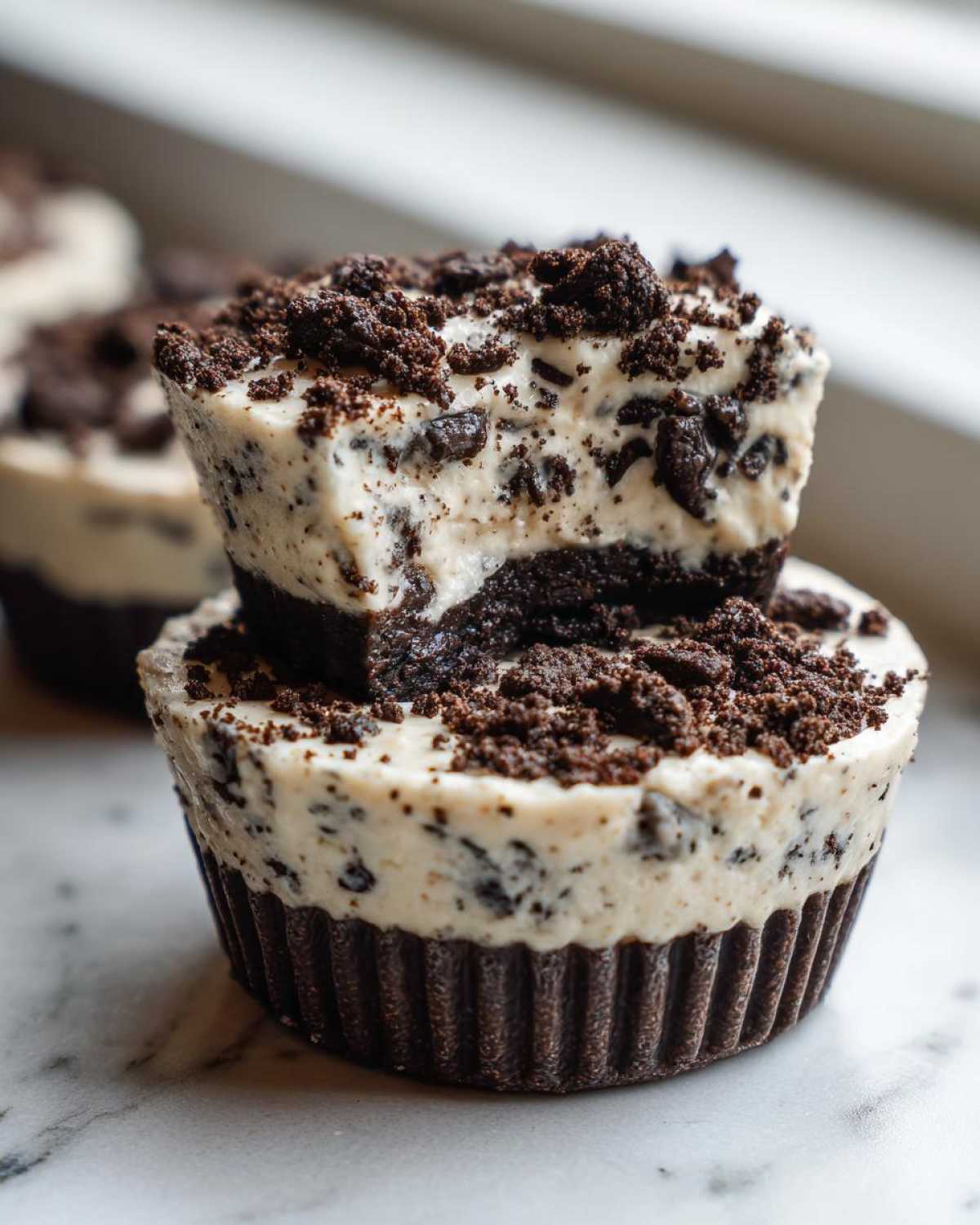 Two stacked No-Bake Cookies and Cream Pie Cups featuring a creamy filling with cookie pieces and a dark chocolate crust.