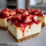 A close-up of a square slice of No-Bake Strawberry Lemon Cheesecake Bars with a thick graham cracker crust and topped with fresh strawberries and glaze.