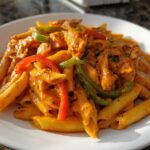 A close-up shot of a serving of vibrant Rasta Pasta featuring penne noodles, chicken pieces, and colorful bell peppers in a creamy sauce.