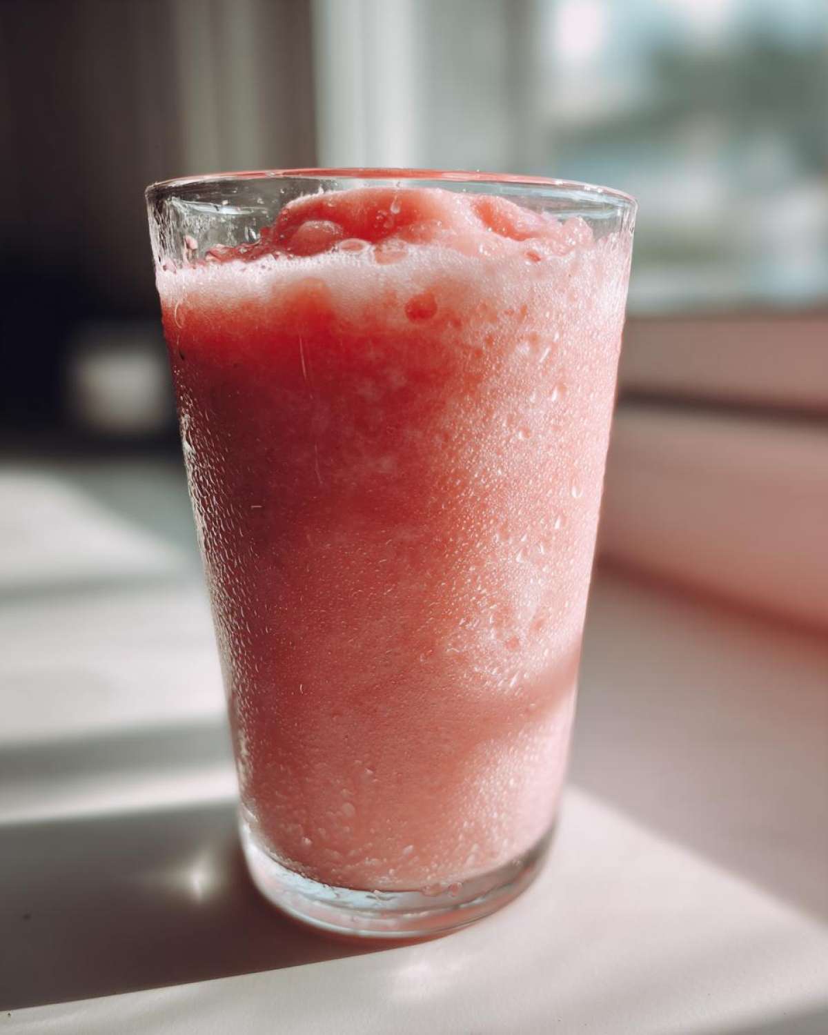 Close-up of a frosty, pink watermelon smoothie in a tall glass, showing condensation droplets on the exterior.