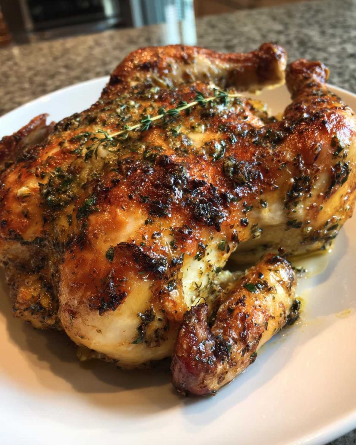 A whole roasted spatchcock chicken with crispy, herb-coated skin resting on a white plate.