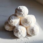 A stack of soft, powdered sugar-dusted cool whip cookies catching bright sunlight.