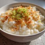 A close-up of creamy Vegan Creamy Coconut Rice Pudding topped with toasted coconut flakes and lime zest.