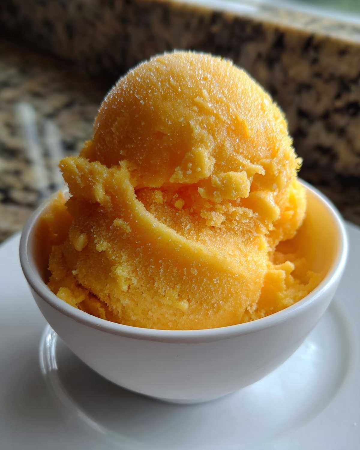 Close-up of two scoops of bright orange Vegan Mango Pineapple Sorbet in a small white bowl.