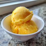 Two scoops of bright yellow Vegan Mango Pineapple Sorbet served in a small white bowl.
