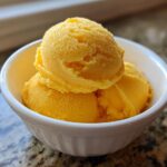 Two scoops of bright orange Vegan Mango Pineapple Sorbet served in a small white bowl.