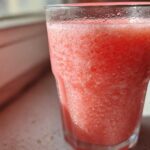 Close-up of a frosty, bright pink watermelon smoothie in a clear glass, showing condensation.