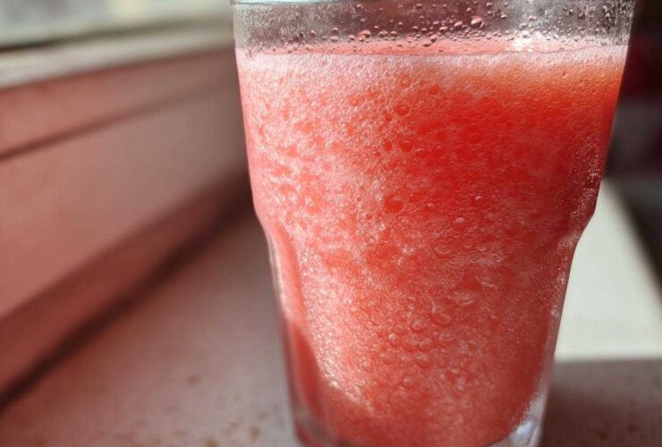 Close-up of a frosty, bright pink watermelon smoothie in a clear glass, showing condensation.