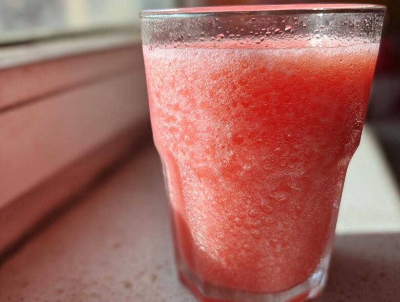 Close-up of a frosty, bright pink watermelon smoothie in a clear glass, showing condensation.