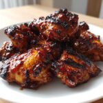 Close-up of several pieces of glossy, caramelized Authentic Huli Huli Chicken piled on a white plate.