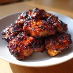 Close-up of several pieces of glistening, caramelized Authentic Huli Huli Chicken piled on a white plate.