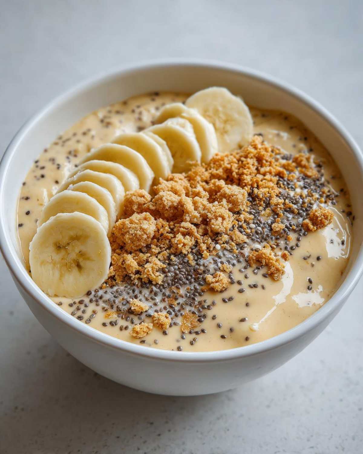 Close-up of a creamy Banana Cream Pie Blended Chia pudding topped with sliced bananas, chia seeds, and graham cracker crumbs.