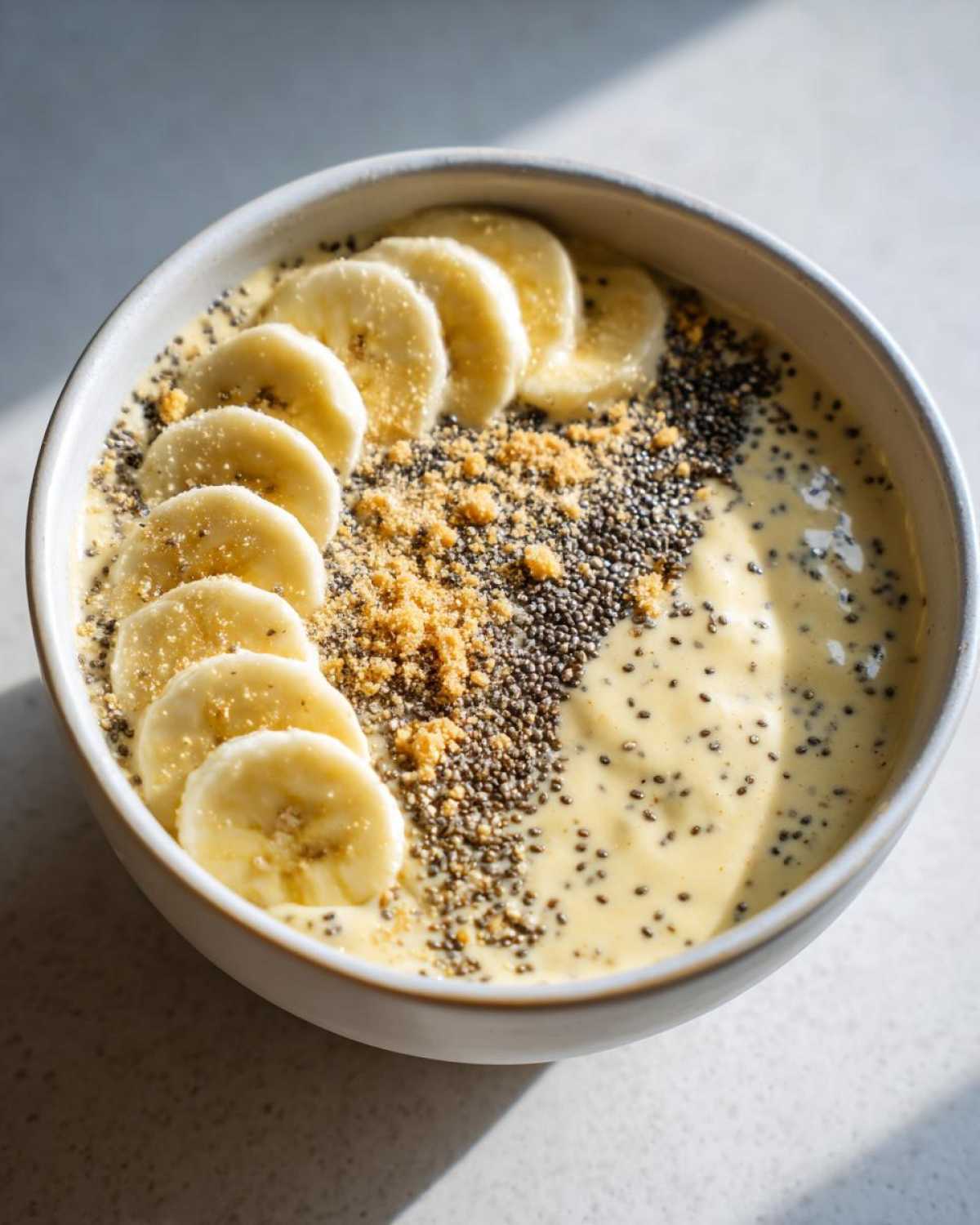 A bowl of creamy Banana Cream Pie Blended Chia topped with sliced bananas, chia seeds, and graham cracker crumbs.