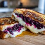Close-up of a perfectly grilled Blueberry Grilled Cheese sandwich cut in half, showing melted cheese and rich blueberry filling.