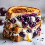 Close-up of a stacked Blueberry Grilled Cheese sandwich with melted cheese and bursting blueberries oozing out.