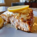 Close-up of a flaky, cooked piece of Boursin Salmon topped with melted cheese and a slice of fresh lemon.