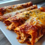 Close-up of three rolled Joanna Gaines Enchiladas covered in red sauce and melted cheese, showing shredded chicken filling.