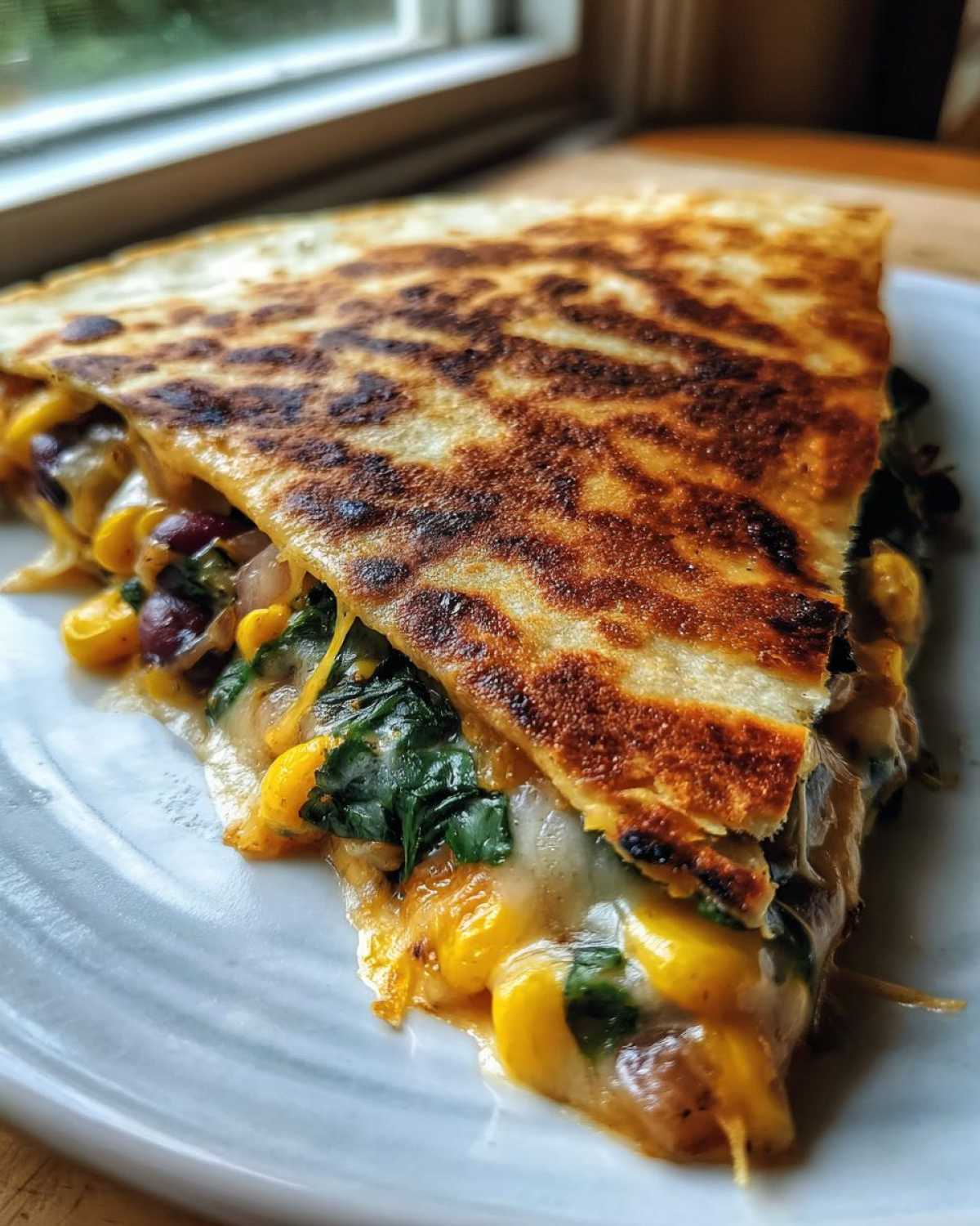 A close-up of a perfectly grilled slice of Vegetarian Quesadillas oozing with melted cheese, corn, black beans, and spinach.