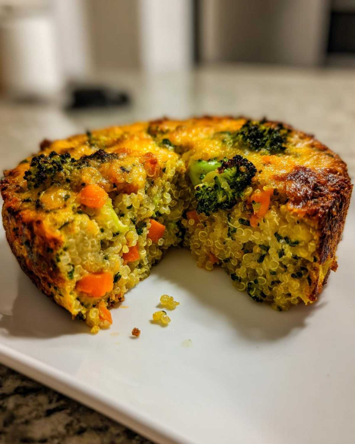 A round, baked slice of Cheesy Veggie Quinoa Casserole showing quinoa, bright orange carrots, and green broccoli florets.