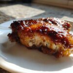 Close-up of a juicy, glazed Chipotle Honey Chicken Thighs piece on a white plate.